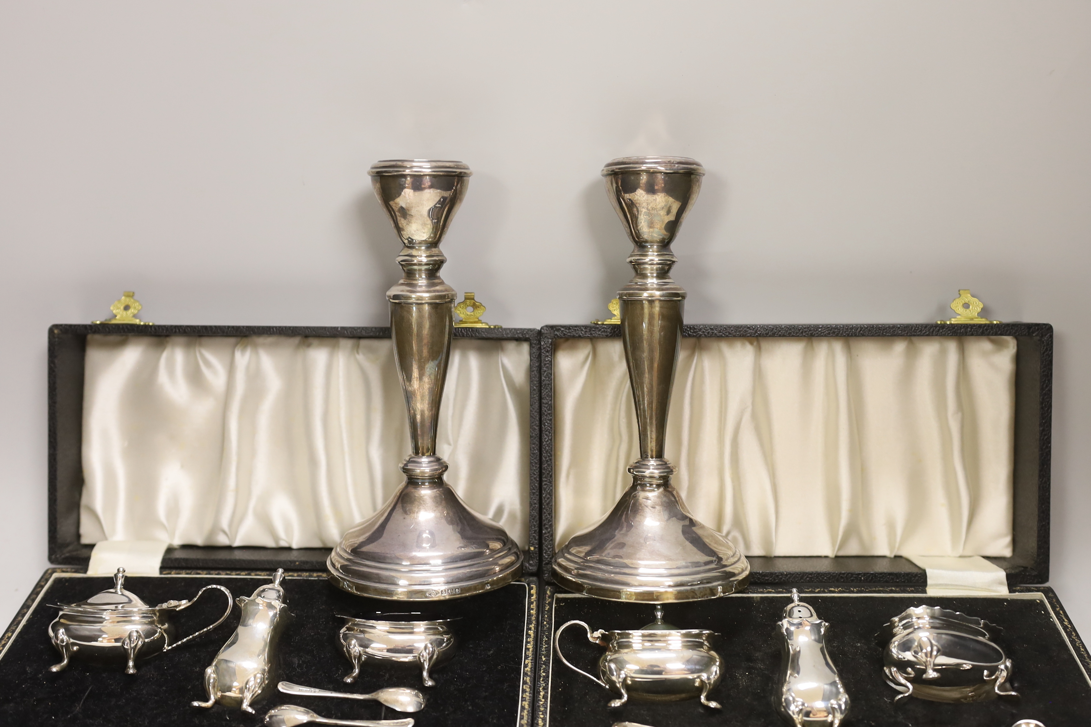 Two modern cased silver three piece cruet sets, with spoons and a pair of modern silver candlesticks, 19.5cm, weighted.